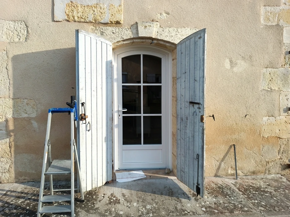 Façade en pierre calcaire avec une porte d'entrée neuve blanche à vitrage divisé 6 carreaux, cintre plein en tête, encadrement arrondi en pierre de taille