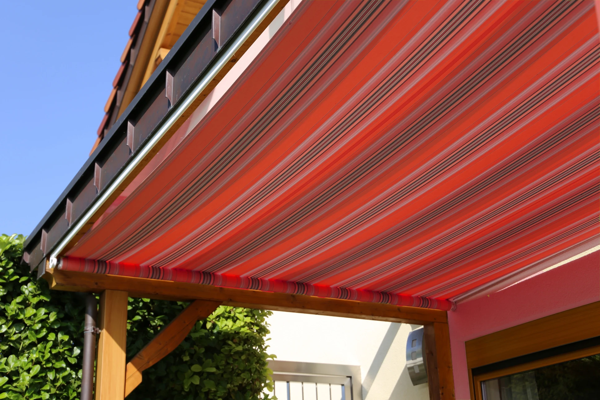 Ouvrier en salopette rouge et casquette installant ou réparant un store à lamelles métalliques sur une terrasse couverte