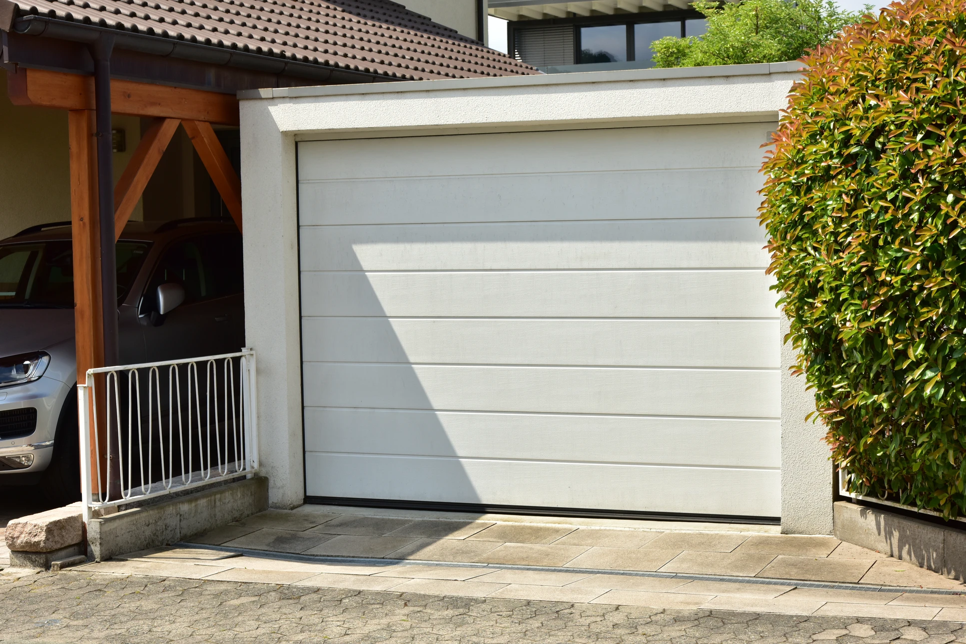 Garage résidentiel moderne avec porte sectionnelle blanche en cours d'ouverture, système de rails et motorisation apparent au plafond
